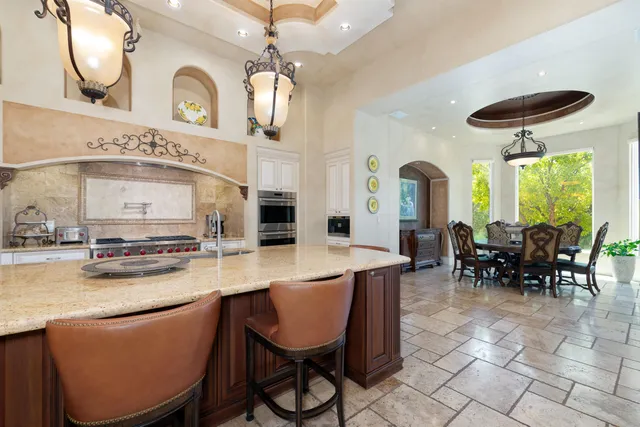 a kitchen with stainless steel appliances kitchen island granite countertop a table chairs sink and cabinets