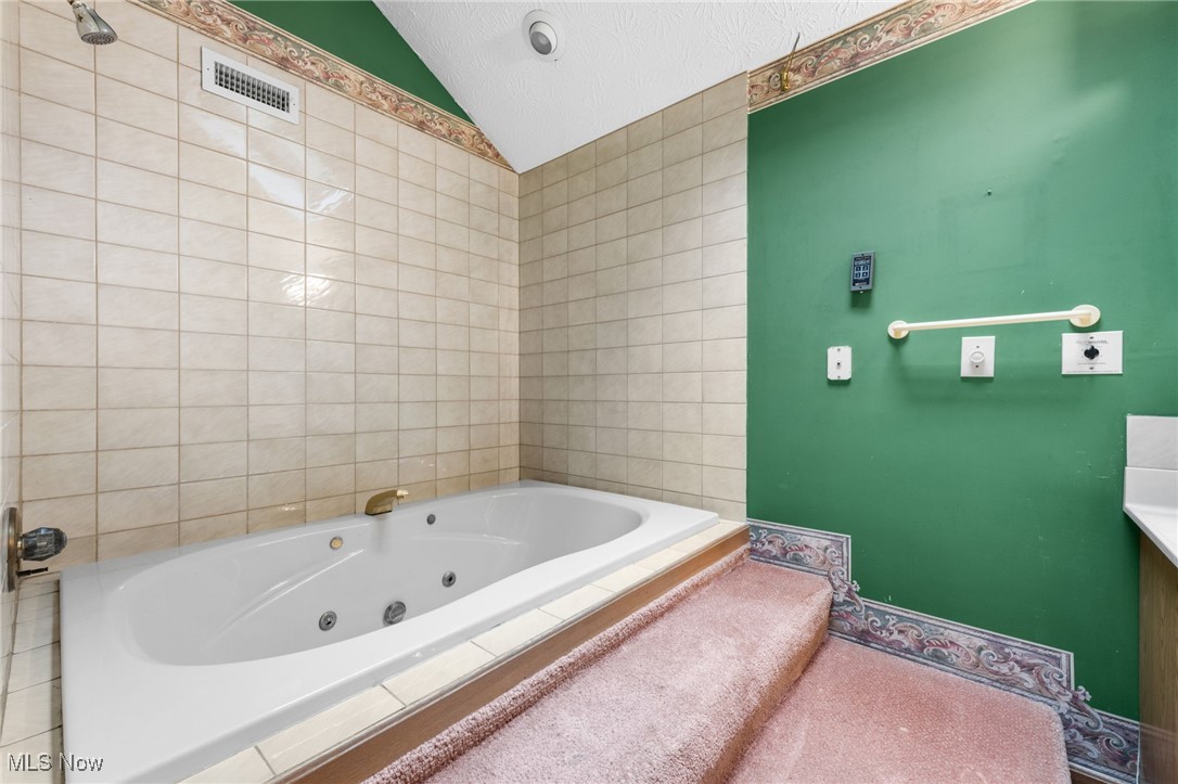 163 Burns Road Elyria, OH 44035 - Photo 18 of 37 Primary bathroom featuring lofted ceiling, a tub with jets, tile walls, and a textured ceiling