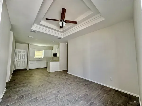 a view of a big room with wooden floor a ceiling fan and kitchen space