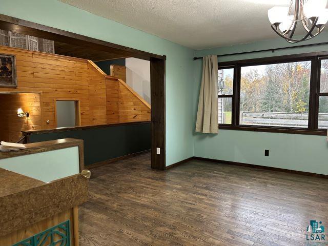 8353 Mannik Road Iron River, WI 54847 - Photo 26 of 48 Unfurnished dining area with dark wood-style floors, a chandelier, a textured ceiling, and wooden walls