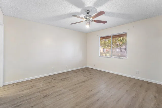 a view of an empty room with chandelier fan and wooden floor