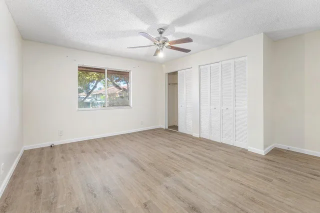 a view of an empty room with wooden floor and a ceiling fan