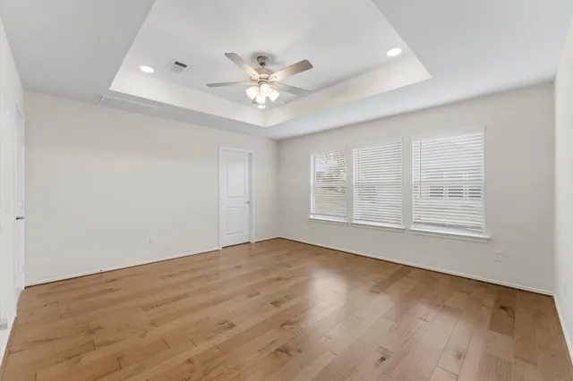 an empty room with wooden floor fan and windows