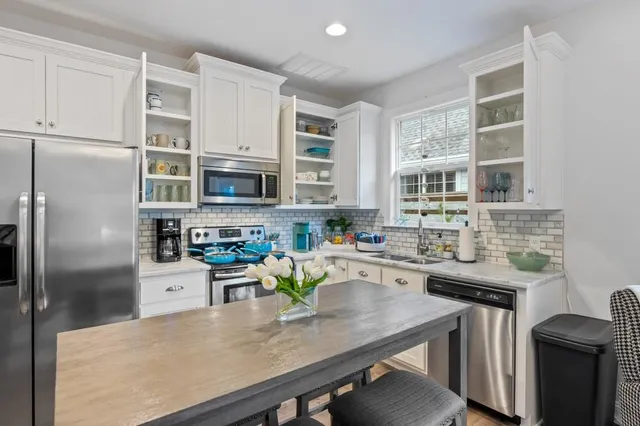 a kitchen with stainless steel appliances a sink a stove a refrigerator cabinets and a dining table