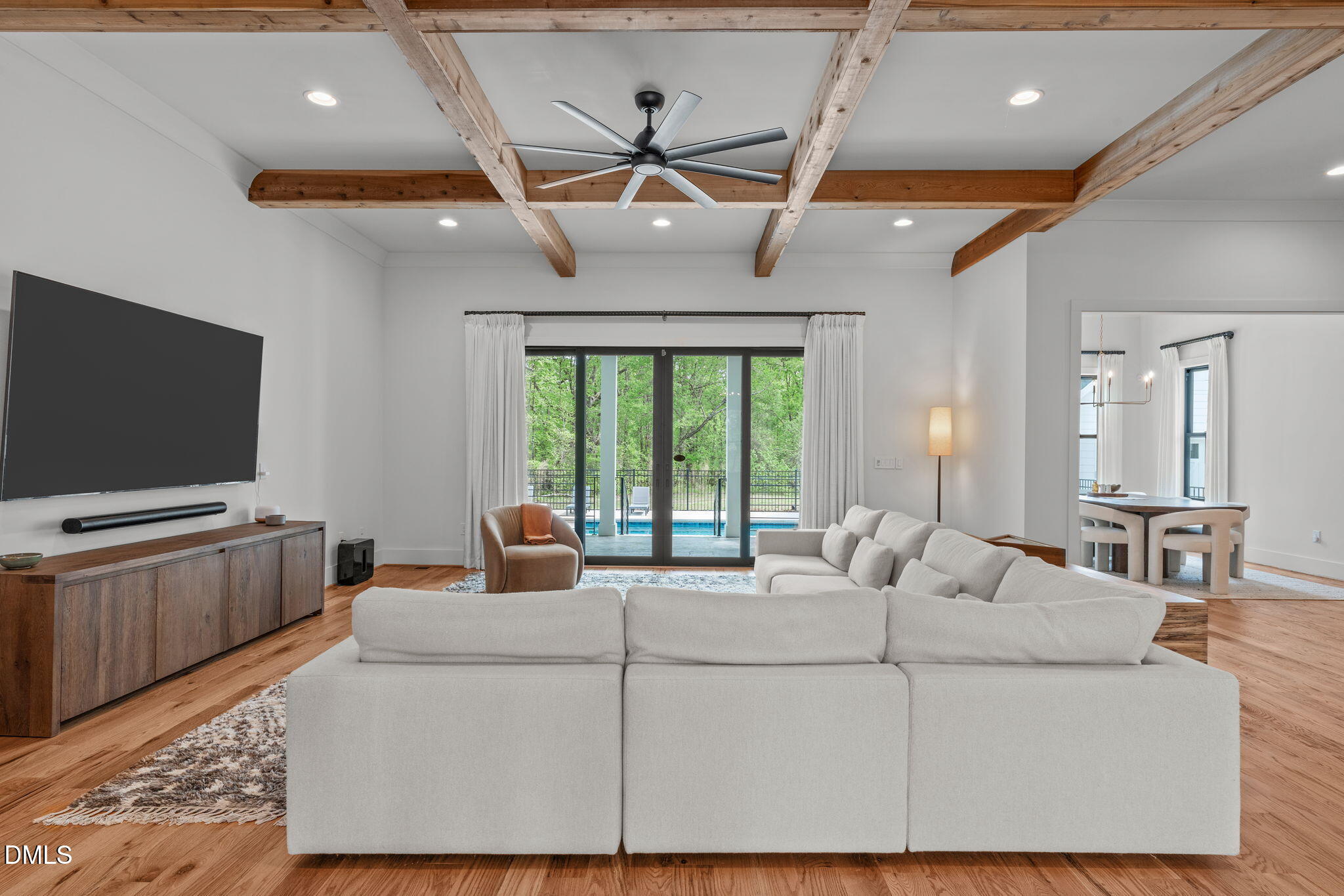 Coffered ceiling, modern ceiling fan, sliding doors to covered deck, patio, and pool, views of trees.