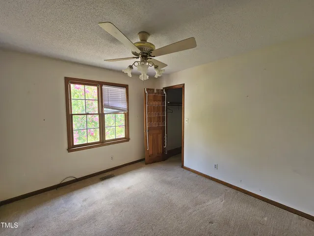 an empty room with chandelier fan and windows