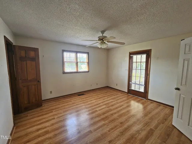 an empty room with wooden floor ceiling fan and windows