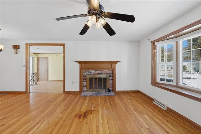 a view of an empty room with wooden floor fireplace and a window