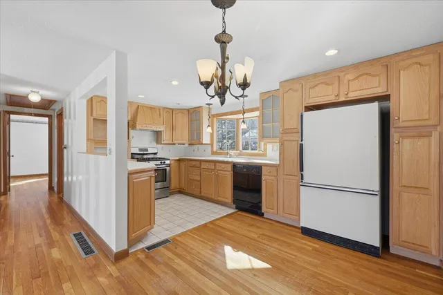 a kitchen with stainless steel appliances granite countertop a refrigerator a sink dishwasher a stove and a dining table with wooden floor