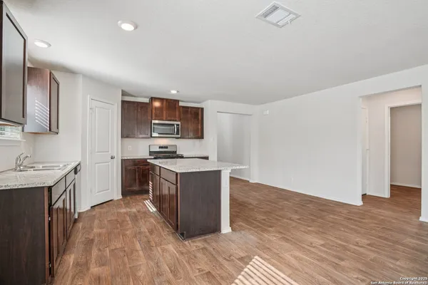 a kitchen with stainless steel appliances granite countertop a stove top oven a sink dishwasher and a refrigerator with wooden floor