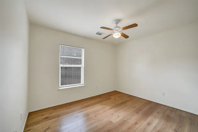 an empty room with wooden floor ceiling fan and windows