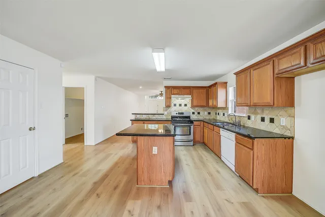 a large kitchen with stainless steel appliances kitchen island granite countertop wooden floors and view living room
