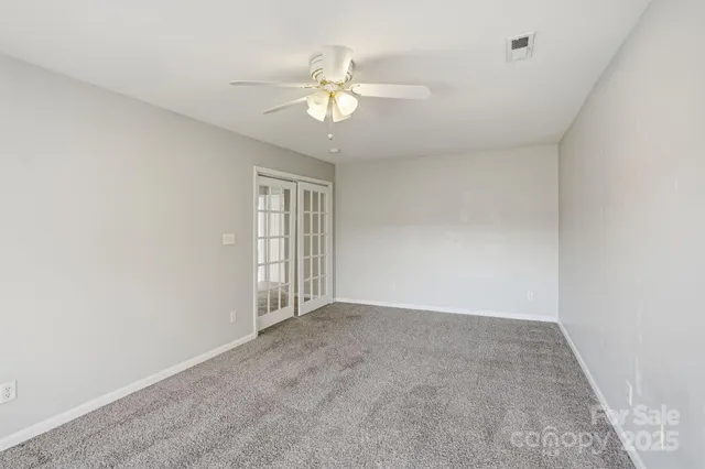 an empty room with a chandelier fan and windows