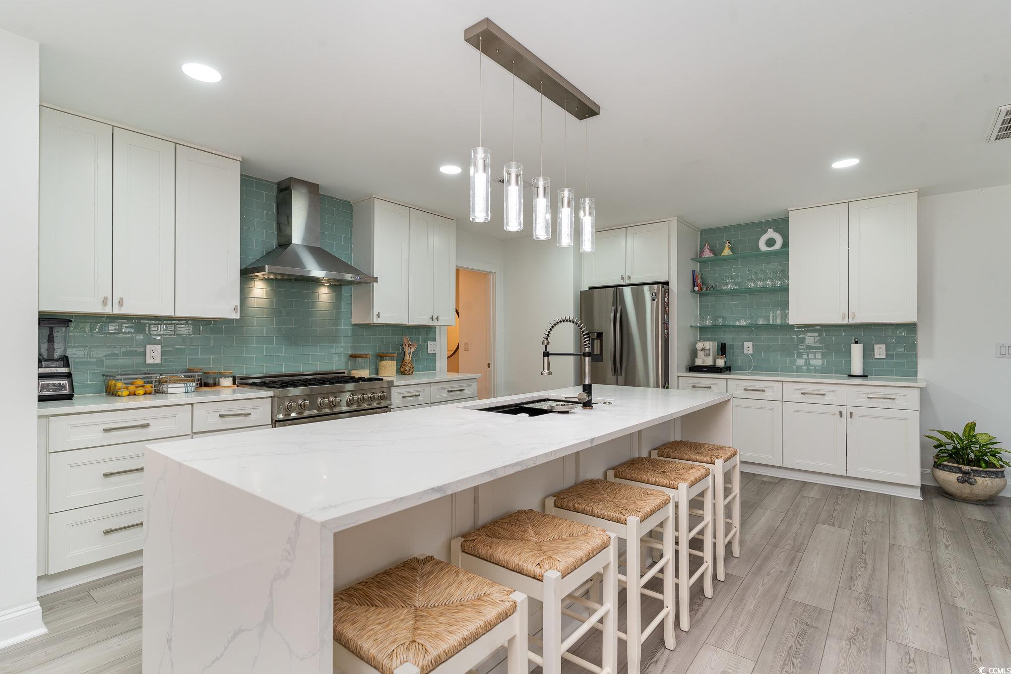 5811 Sumter Drive Myrtle Beach, SC 29577 - Photo 8 of 39 Kitchen featuring tasteful backsplash, a kitchen bar, wall chimney exhaust hood, decorative light fixtures, and light wood-type flooring