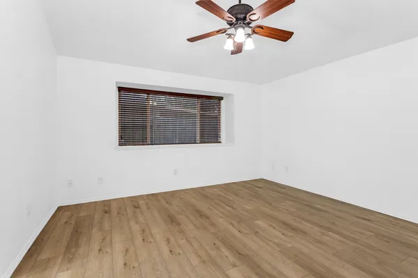 an empty room with wooden floor chandelier fan and windows