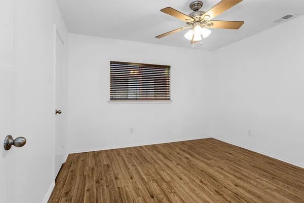 an empty room with a chandelier fan and wooden floor