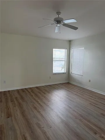 an empty room with wooden floor ceiling fan and windows