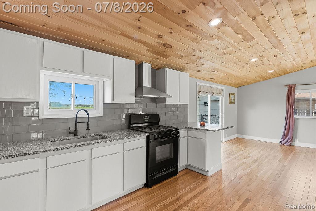 5698 McGrandy Road Bridgeport, MI 48722 - Photo 15 of 26 Modern kitchen featuring white cabinetry, granite-style countertops, a stainless steel range hood, and a gray subway tile backsplash