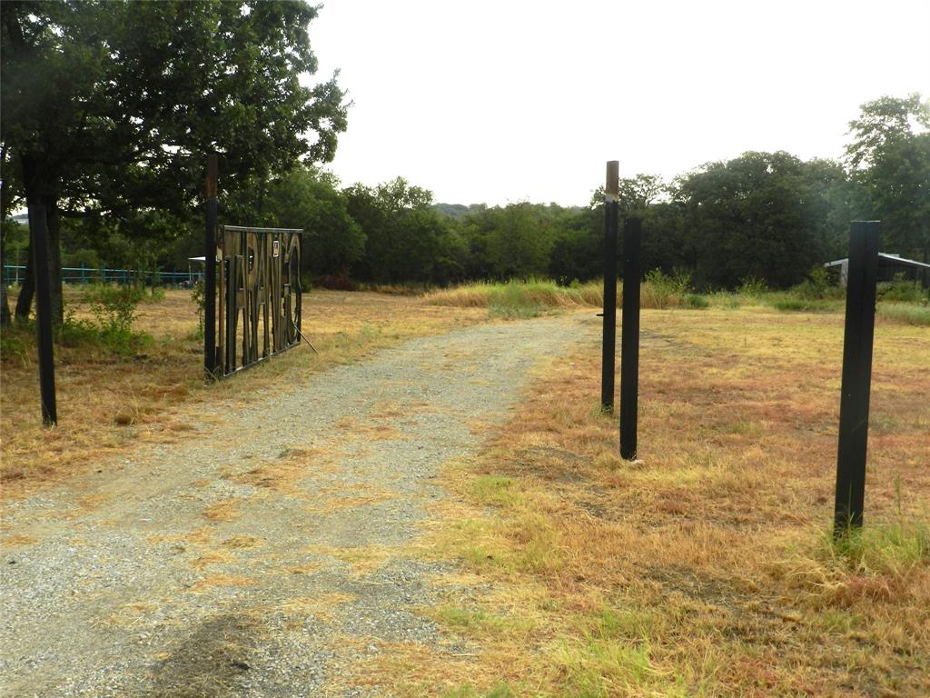 588 Salt Creek Road Springtown, TX 76082 - Photo 2 of 19 Gravel driveway with a decorative gate, bordered by mature trees and natural landscaping