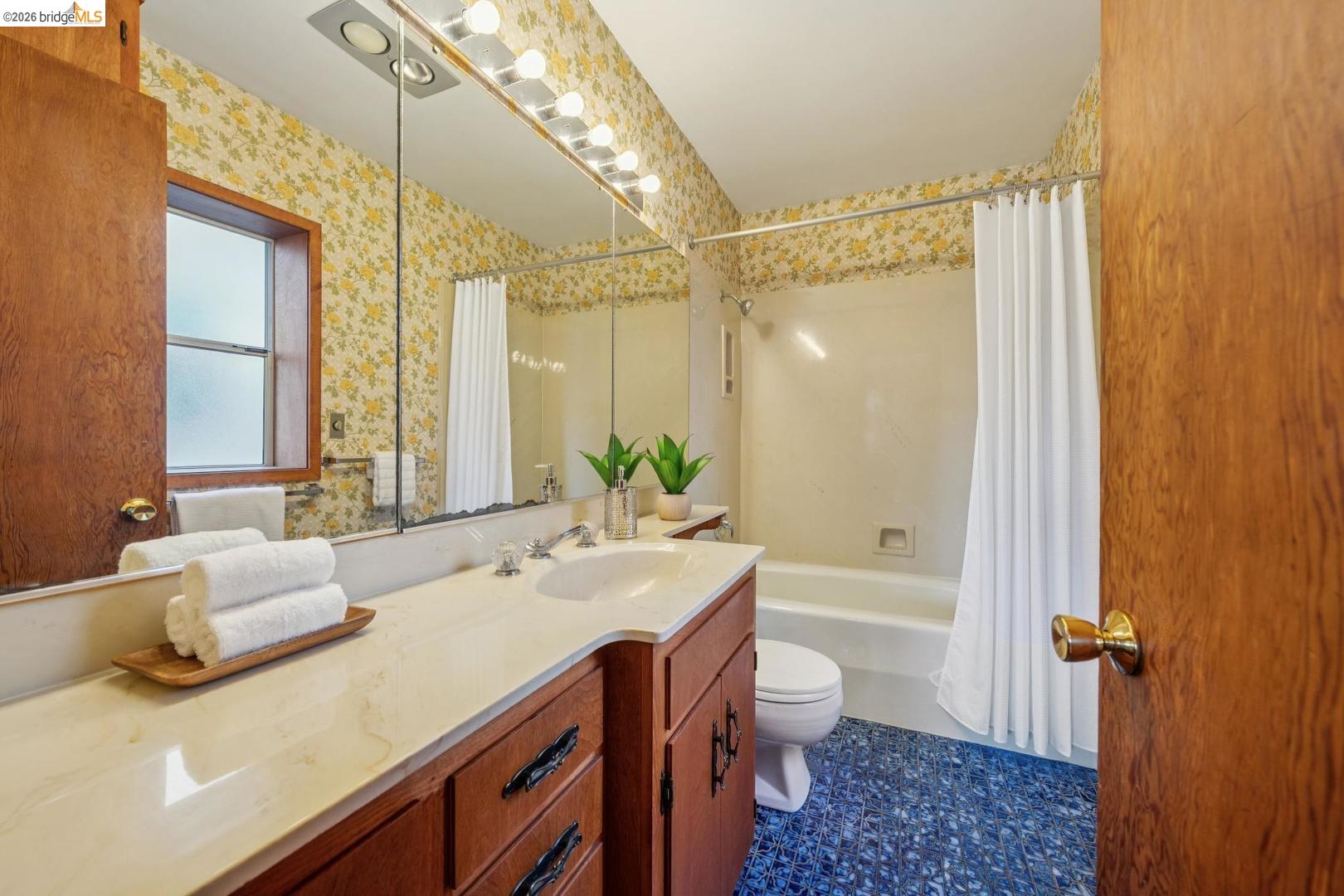 155 Avenida Drive Berkeley, CA 94708 - Photo 52 of 86 Built-in vanity with an integrated sink and light-colored countertop, large wall-mounted mirror, overhead vanity lighting, window with frosted glass, and a bathtub with a shower curtain