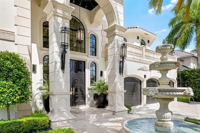 a view of a swimming pool with lawn chairs under an umbrella with potted plants and large trees