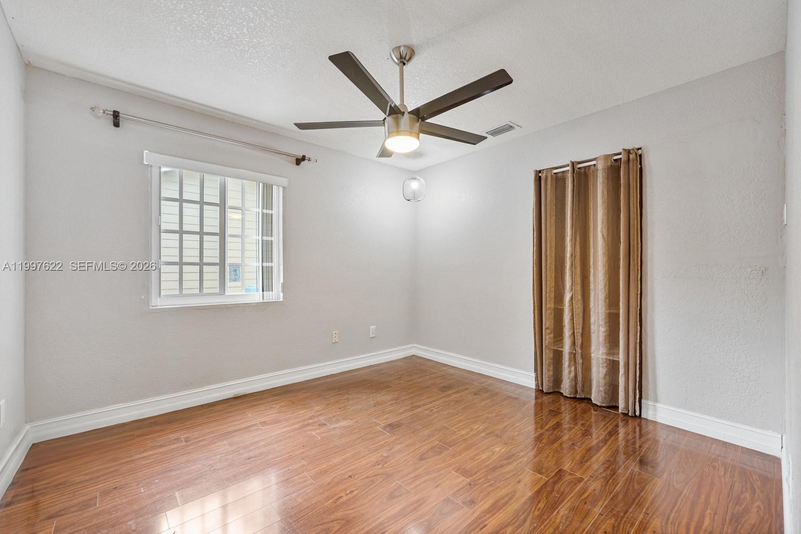 14912 Southwest 143rd Court, Unit 14912 Miami, FL 33186 - Photo 29 of 35 an empty room with wooden floor ceiling fan and windows