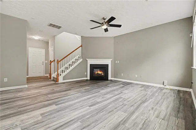a view of an empty room with wooden floor a ceiling fan and a fireplace