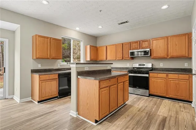 a kitchen with stainless steel appliances granite countertop a stove top oven a sink dishwasher and a microwave oven on the wooden floor