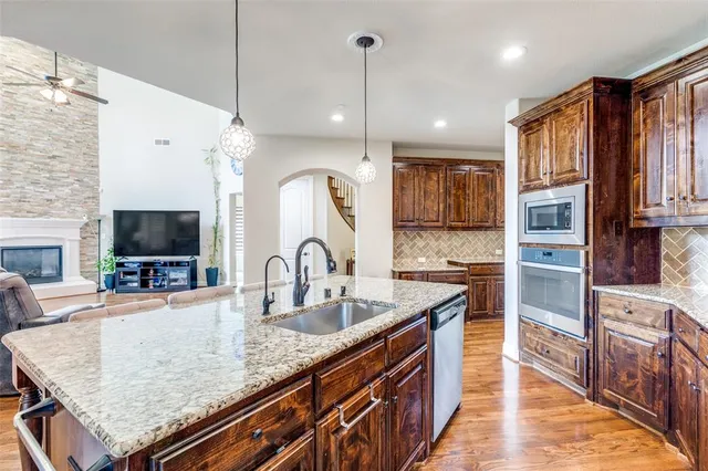 a kitchen with stainless steel appliances kitchen island granite countertop a refrigerator a stove a sink a dining table and chairs with wooden floor