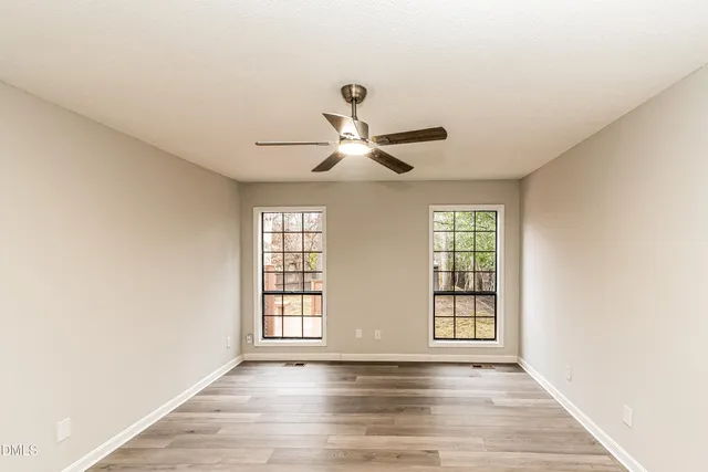an empty room with wooden floor chandelier fan and windows