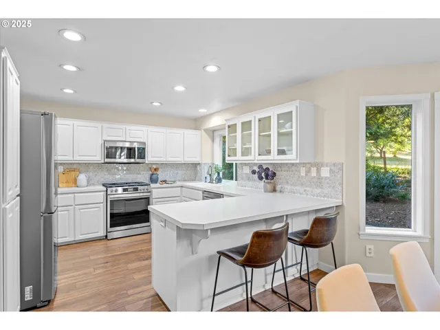 a kitchen with stainless steel appliances kitchen island granite countertop a stove a sink a refrigerator and white cabinets with wooden floor