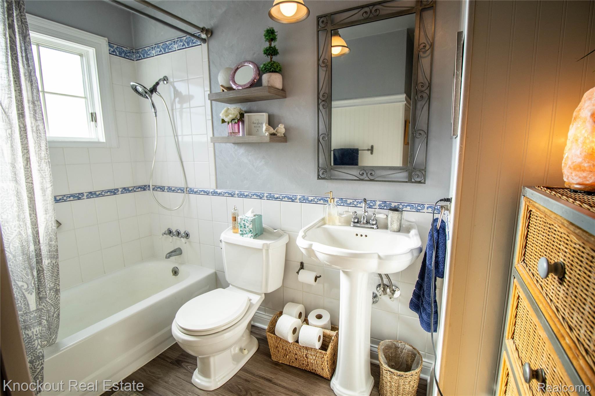 14720 Lincoln Road Chesaning, MI 48616 - Photo 34 of 60 Bright, well-appointed bathroom featuring a pedestal sink with chrome fixtures, white subway tile with decorative blue border trim, and a bathtub-shower combination with curtain enclosure