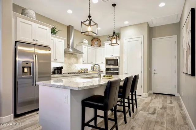 a kitchen with stainless steel appliances granite countertop a refrigerator a sink dishwasher a dining table and chairs with wooden floor