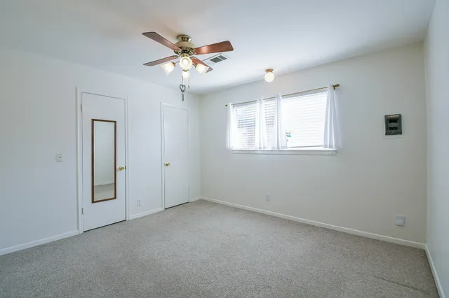 an empty room with a chandelier fan and wooden floor