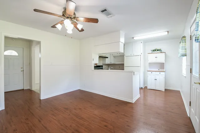 an empty room with wooden floor chandelier fan and windows