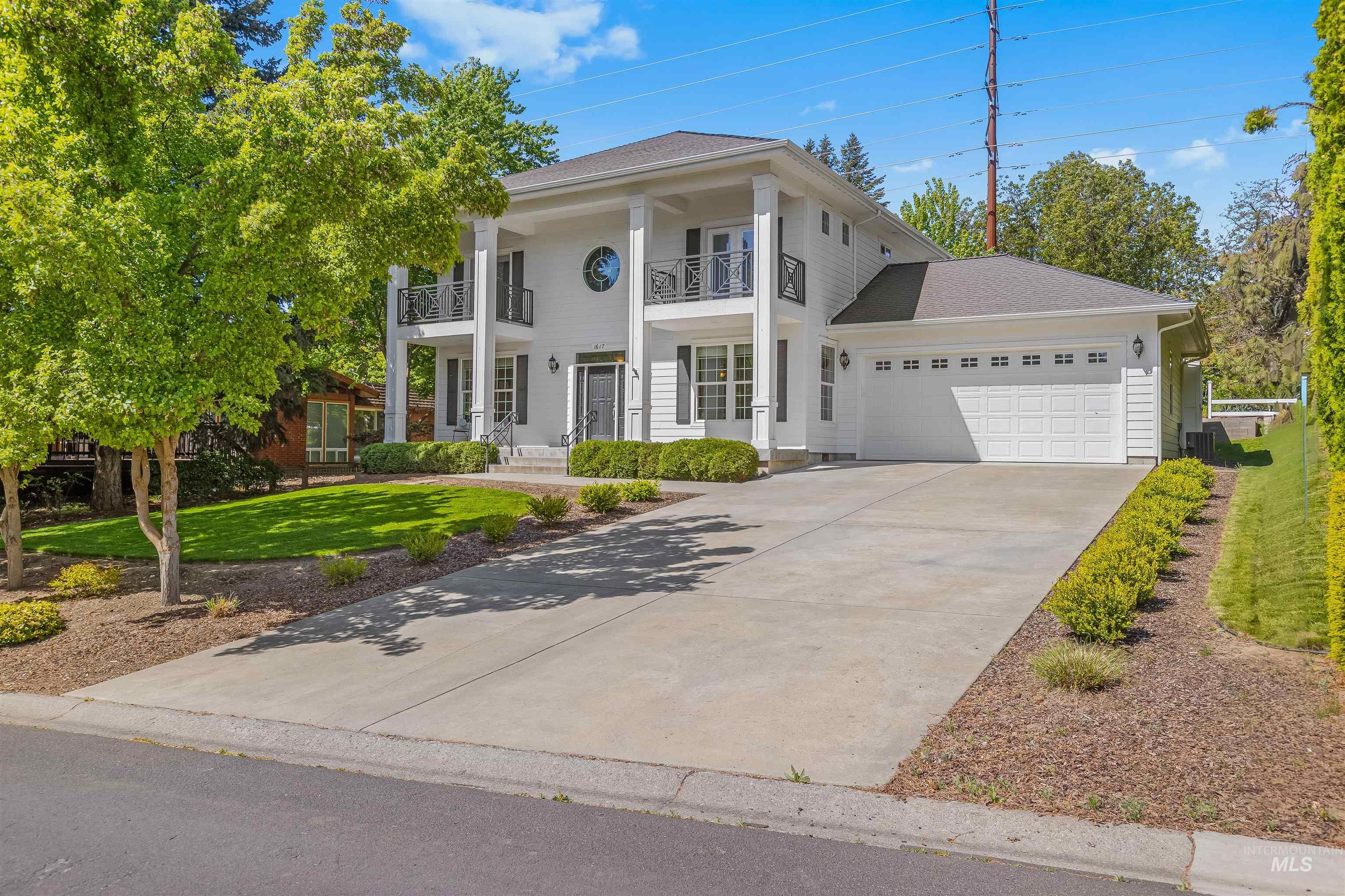 1617 Pine Cone Road Moscow, ID 83843 - Photo 2 of 44 Two-story Colonial-style residence featuring a prominent portico with white columns, two second-story balconies with black railings, a circular window, and a two-car garage with a paneled door