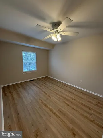 an empty room with wooden floor ceiling fan and windows