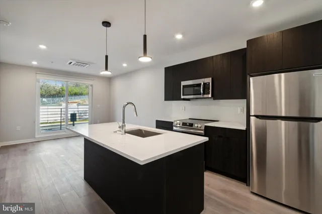 a kitchen with stainless steel appliances a microwave a sink a stove a refrigerator and island with wooden floor