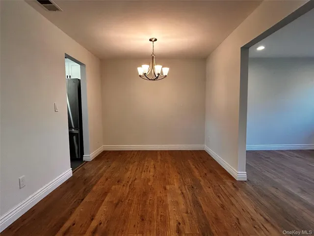 an empty room with wooden floor chandelier and windows