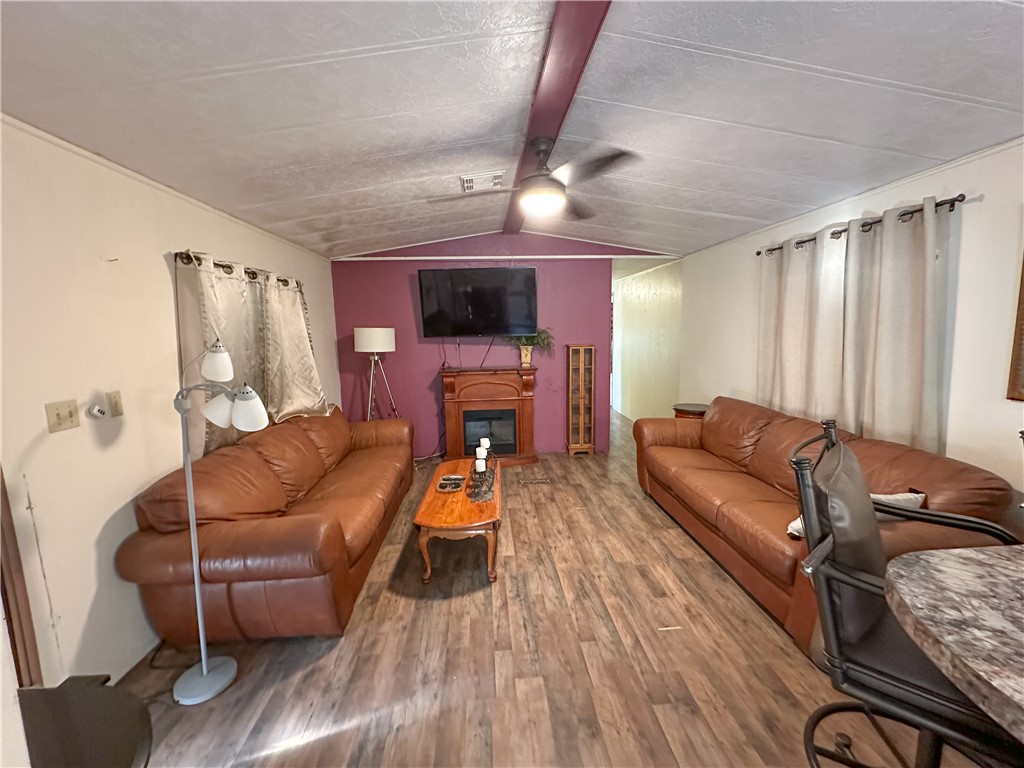 1655 Ramar Road Bullhead City, AZ 86442 - Photo 12 of 49 Living area featuring a glass covered fireplace, wood finished floors, a ceiling fan, and beam ceiling