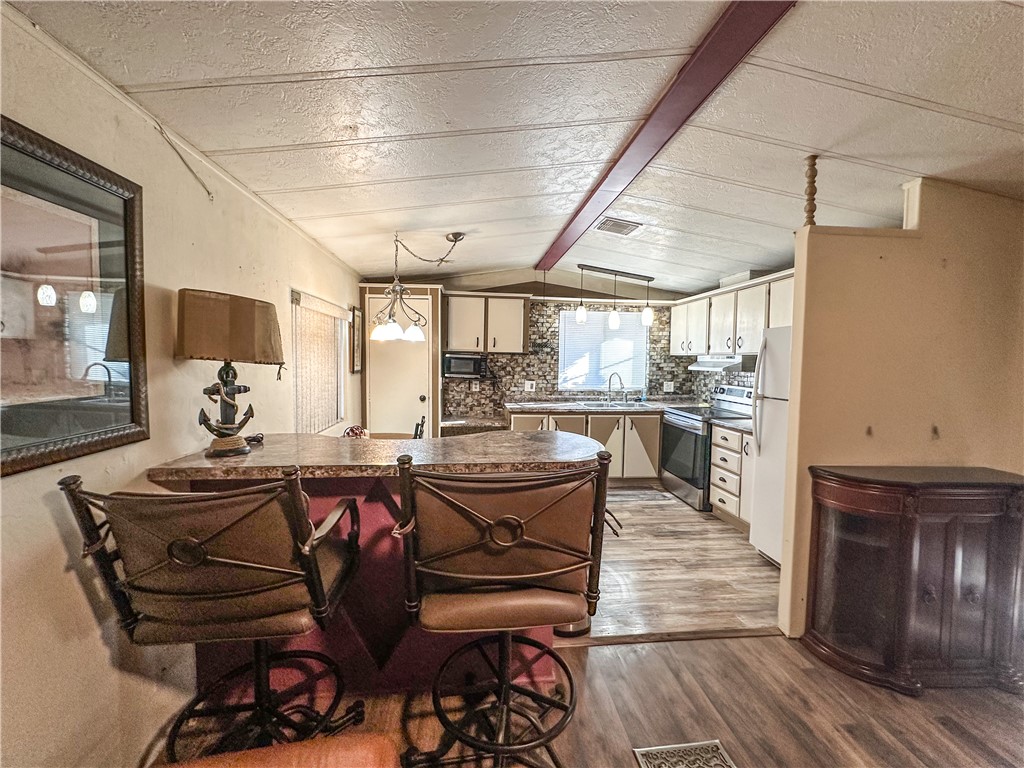 1655 Ramar Road Bullhead City, AZ 86442 - Photo 6 of 49 Kitchen featuring a peninsula, stainless steel appliances, dark wood-style floors, dark countertops, and decorative light fixtures