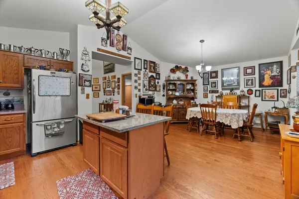 a kitchen with stainless steel appliances granite countertop a refrigerator a sink dishwasher a dining table and chairs with wooden floor