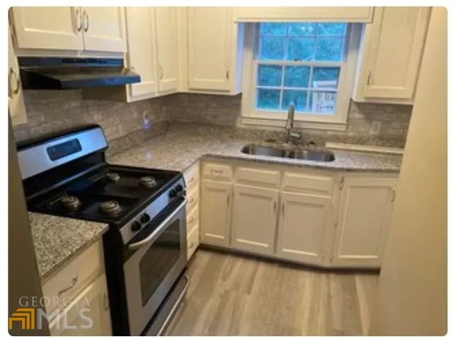 a kitchen with granite countertop a sink a stove and cabinets