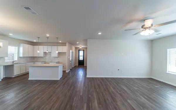 an empty room with wooden floor and kitchen view