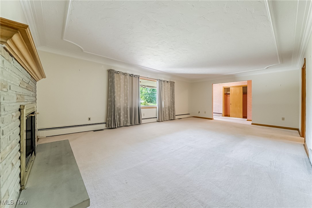 550 Cooper Foster Park Road Lorain, OH 44053 - Photo 7 of 50 Unfurnished living room with ornamental molding, a glass covered fireplace, baseboard heating, light carpet, and a textured ceiling
