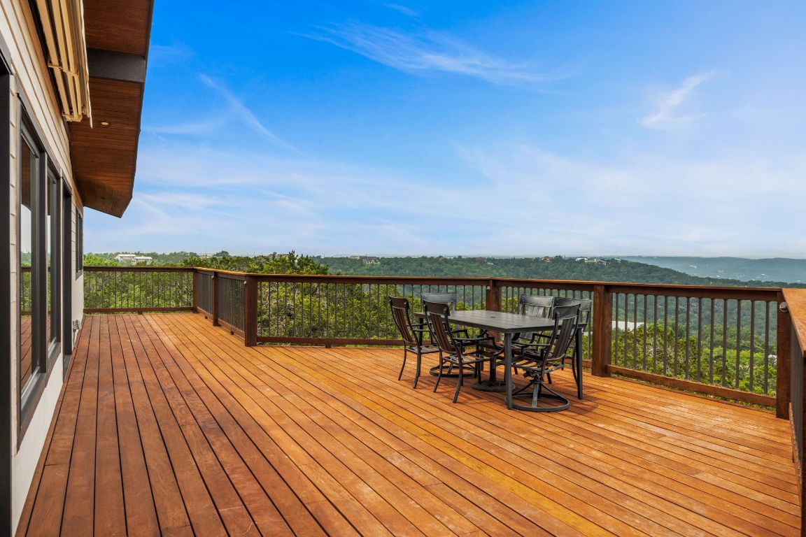 a view of a roof deck with table and chairs a barbeque with wooden floor and fence
