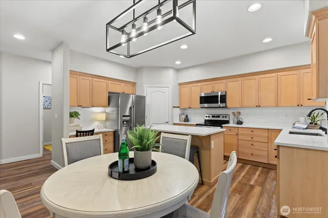 a kitchen with stainless steel appliances granite countertop a refrigerator a stove a sink dishwasher a dining table and chairs with wooden floor