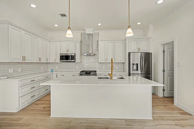 a large white kitchen with kitchen island a sink a stove a refrigerator and white cabinets with wooden floor