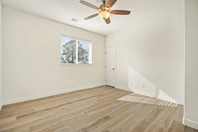 an empty room with wooden floor fan and windows