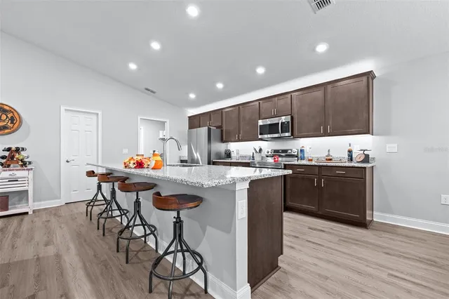 a kitchen with stainless steel appliances granite countertop a refrigerator a stove a sink a dining table and chairs with wooden floor